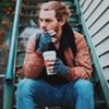 Man sitting, drinking coffee, and smoking outside.