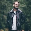 Man in leather jacket in forest setting.