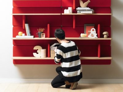 Person organizing items on red wall shelf.