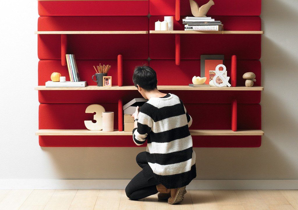 Person organizing items on red wall shelf.