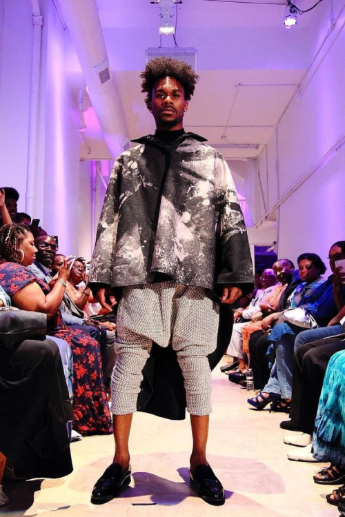 Model walking runway in artistic fashion outfit.