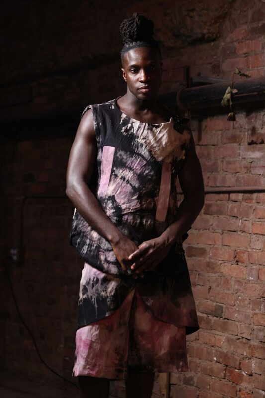 Man in tie-dye outfit against brick wall.