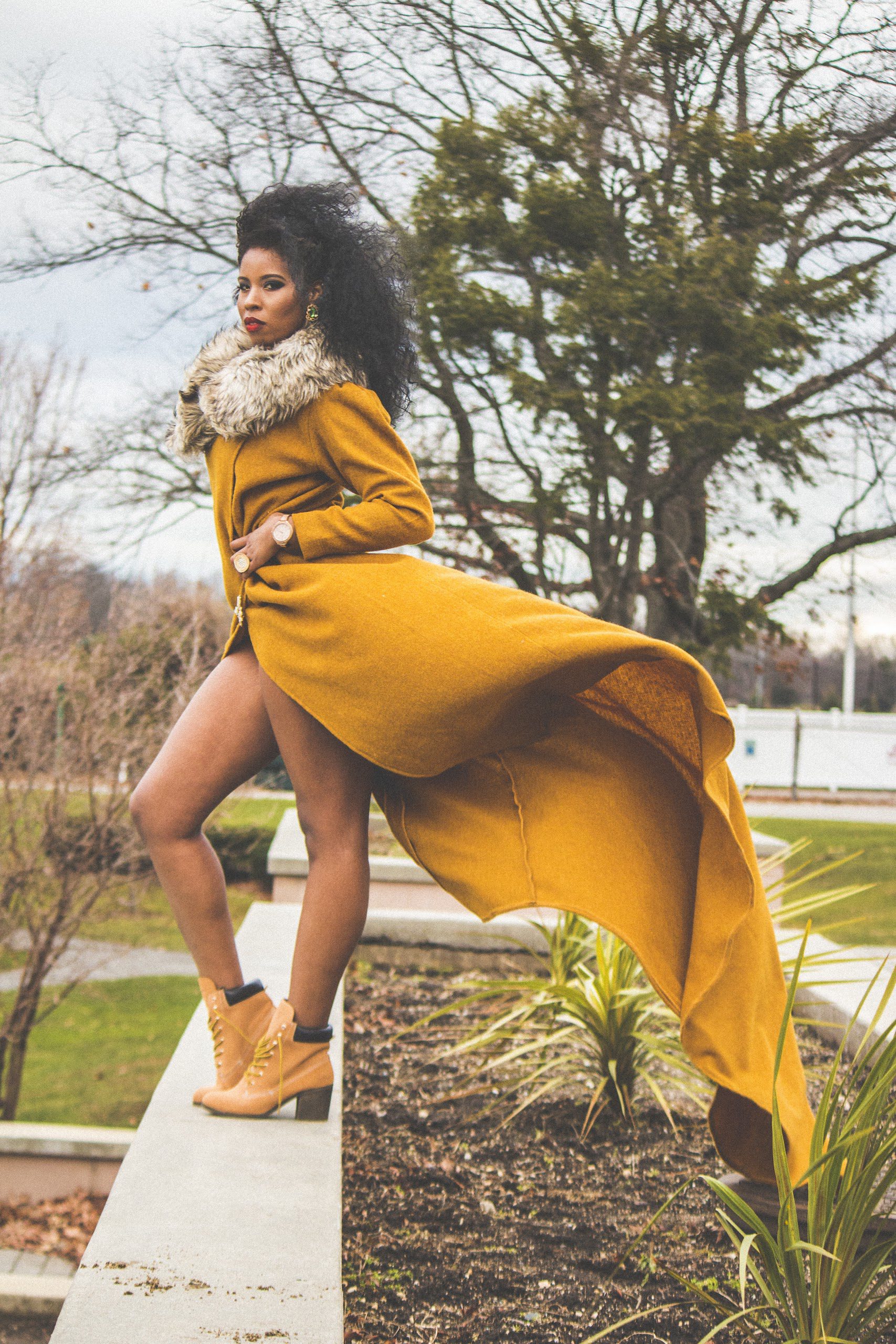 Woman in yellow coat posing outdoors.