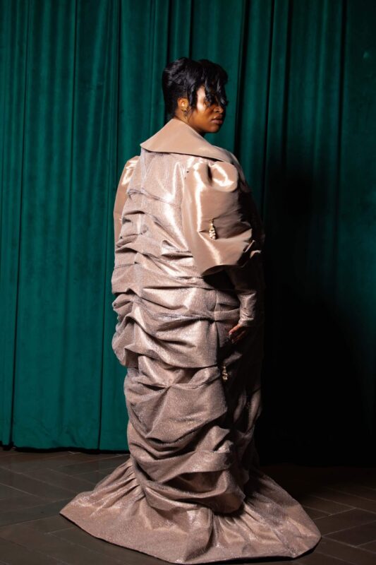 Woman in elaborate, metallic gown, green background.