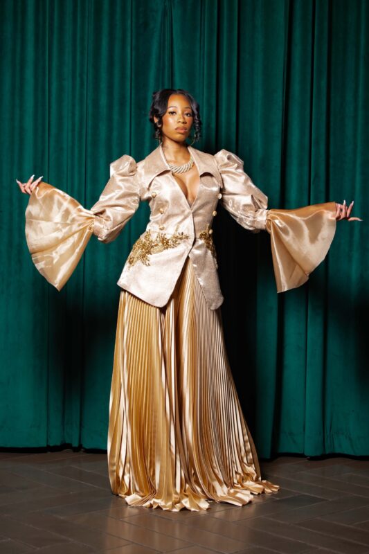 Woman in elegant gold outfit, green curtain.