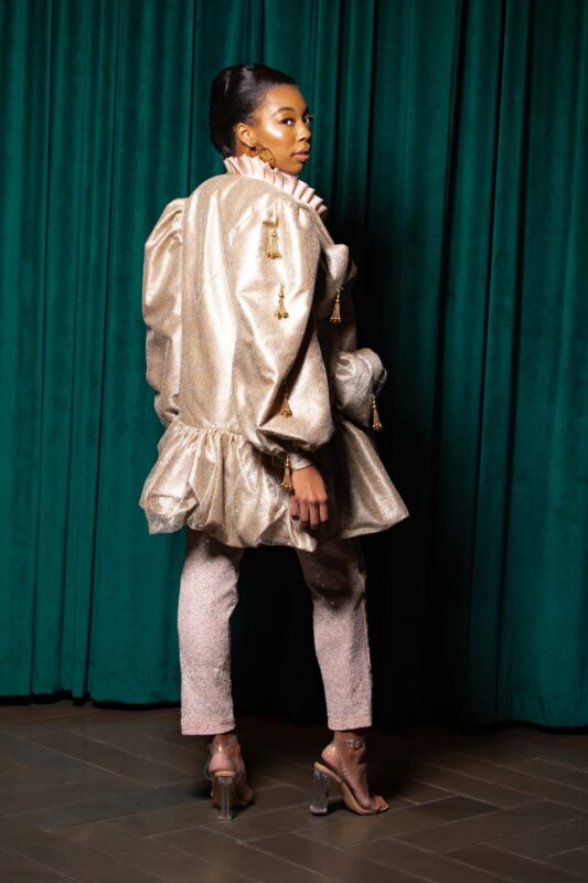Woman in metallic outfit, green curtain background.