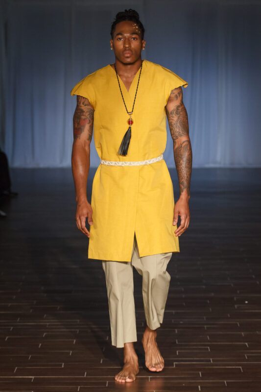 Model in yellow tunic on runway.