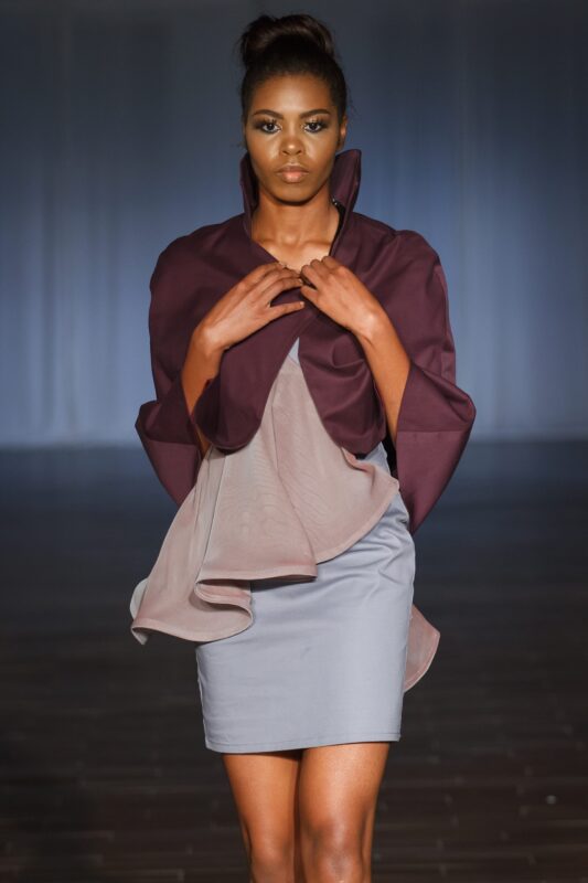 Model in purple and gray outfit walking runway.