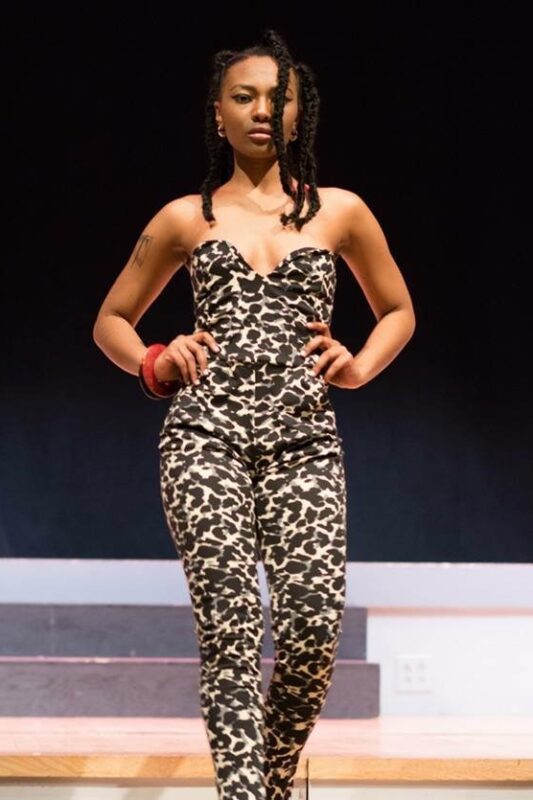 Model in leopard print jumpsuit on runway.